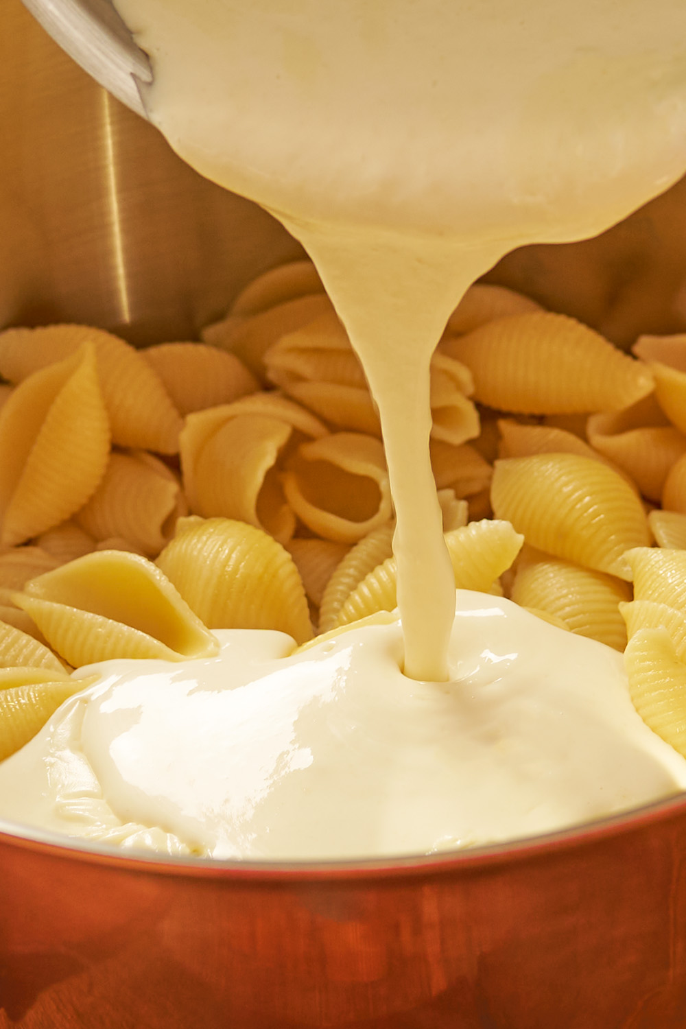 Close-up of creamy cheese sauce poured over pasta shells